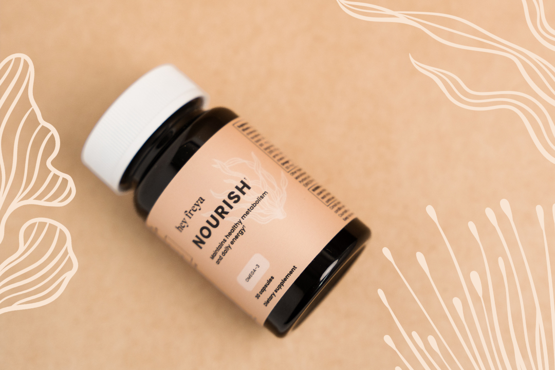 An amber-colored bottle of Hey Freya’s NOURISH multivitamin for women’s health on a peach background